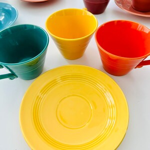 Puede incluir: Un juego de tazas de t&eacute; y platillos coloridos. Las tazas son amarillas, naranjas, verdes y rojas. Los platillos son amarillos, rosados y azules.