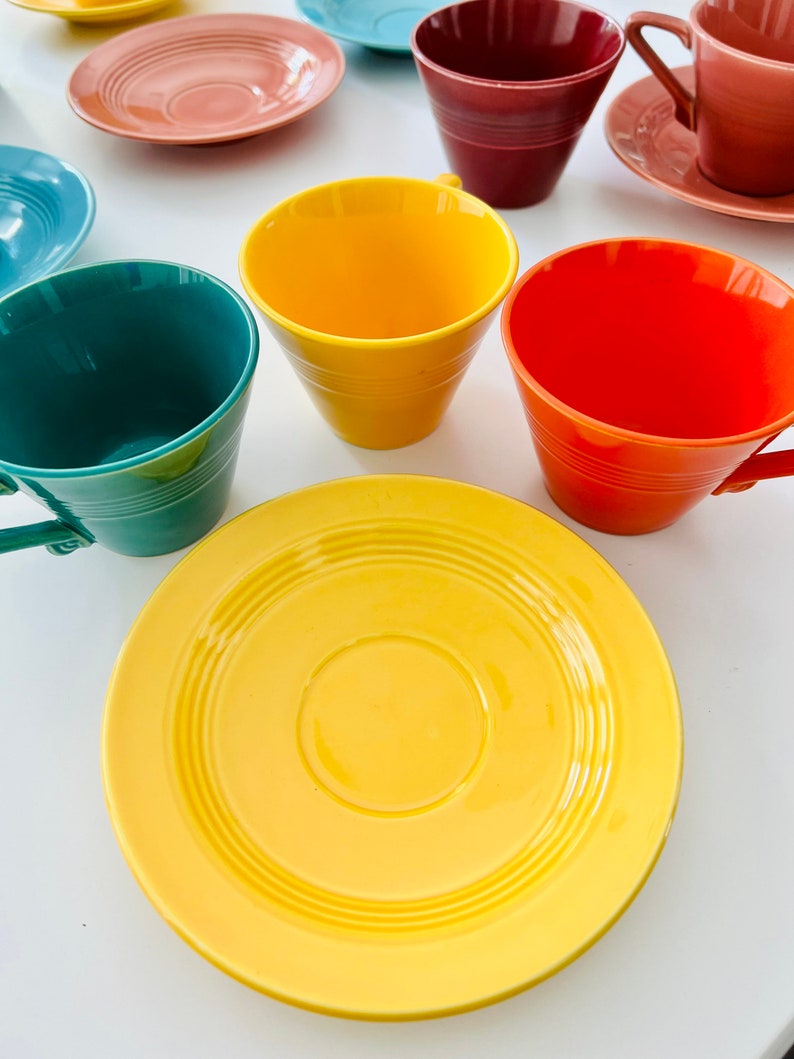 Puede incluir: Un juego de tazas de t&eacute; y platillos coloridos. Las tazas son amarillas, naranjas, verdes y rojas. Los platillos son amarillos, rosados y azules.