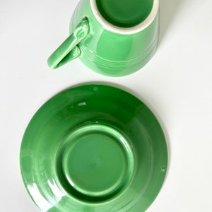 Puede incluir: Un juego de taza y platillo de cer&aacute;mica verde. La taza y el platillo son de un color verde brillante y vibrante. La taza tiene una forma simple y redondeada y una peque&ntilde;a asa. El platillo es ligeramente m&aacute;s grande y tiene un borde ligeramente elevado.