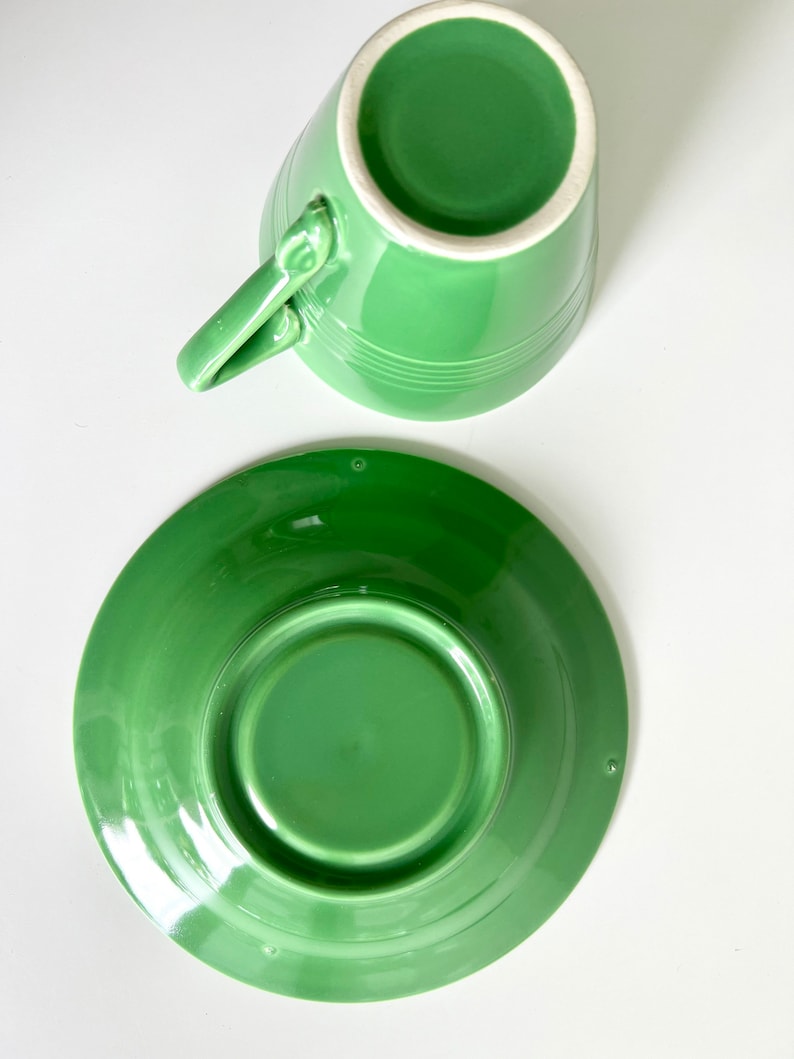 Puede incluir: Un juego de taza y platillo de cer&aacute;mica verde. La taza y el platillo son de un color verde brillante y vibrante. La taza tiene una forma simple y redondeada y una peque&ntilde;a asa. El platillo es ligeramente m&aacute;s grande y tiene un borde ligeramente elevado.