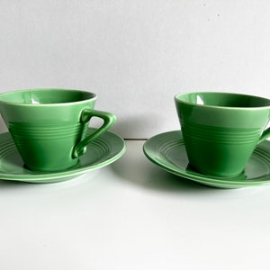 Puede incluir: Dos tazas de t&eacute; verdes y platillos. Las tazas son de color verde claro y tienen un dise&ntilde;o simple. Los platillos son blancos con un borde verde.