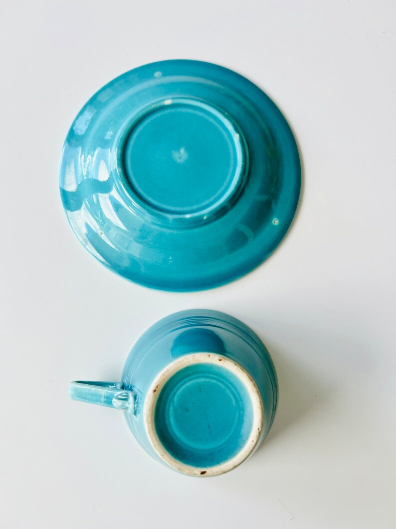 Puede incluir: Un juego de taza y platillo de cer&aacute;mica azul turquesa. La taza tiene un asa y el platillo tiene un borde ligeramente elevado.