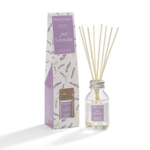 May include: A white box with a purple and white floral design and the text "Hassett Green" and "Just Lavender" on it. A clear glass bottle with a silver lid and a label that says "Hassett Green" and "Just Lavender". The bottle is filled with a clear liquid and has wooden sticks in it.