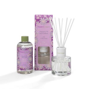 May include: A Hassett Green fragrance oil diffuser set with a refill bottle, reed diffuser, and box. The set includes a bottle of lilac and lavender fragrance oil, a glass diffuser, and white reeds. The box is purple with floral designs.