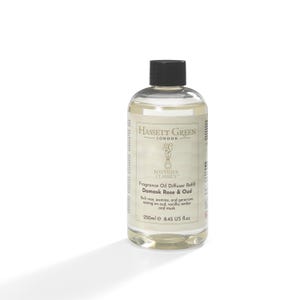 May include: A transparent glass bottle with a black cap, containing a pale liquid. The label displays "HASSETT GREEN LONDON" and "Damask Rose & Oud" fragrance oil diffuser refill. The bottle contains 250ml.
