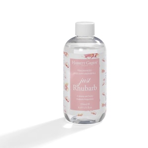 May include: A clear glass bottle with a white cap filled with a clear liquid. The bottle has a pink and white label with the text "HASSETT GREEN" and "just Rhubarb". The label also says "FRAGRANCED REED DIFFUSED REFILL" and "A sharp yet fruity rhubarb fragrance". The bottle contains 250 ml or 8.45 fl oz.