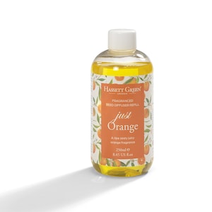 May include: A clear glass bottle containing a yellow liquid. The bottle has a white label with the text "Hassett Green London Fragranced Reed Diffuser Refill Just Orange A ripe zesty juicy orange fragrance 250ml e 8.45 US fl.oz" and a picture of oranges.