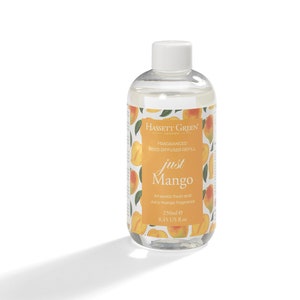 May include: A clear glass bottle with a white cap filled with a clear liquid. The bottle has a label with the text "HASSETT GREEN LONDON FRAGRANCED REED DIFFUSER REFILL just Mango An exotic fresh and juicy mango fragrance 250ml e 8.45 US fl.oz" and a pattern of yellow mangoes on a white background.