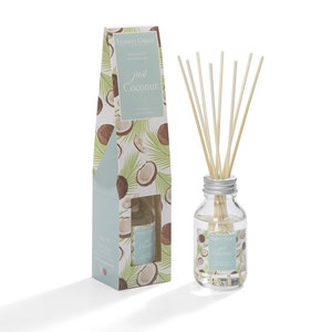 May include: A clear glass bottle with a silver lid filled with a coconut scented diffuser oil and wooden diffuser sticks. The bottle is labelled "Hassett Green" and "Just Coconut". The bottle is sitting on a white surface next to a cardboard box with a similar design.