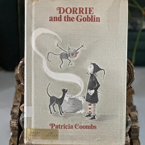 May include: A hardcover book titled Dorrie and the Goblin by Patricia Coombs. The light gray cover features an illustration of a small figure in a black outfit and striped socks, a black cat, a cauldron, and a small goblin with red eyes.