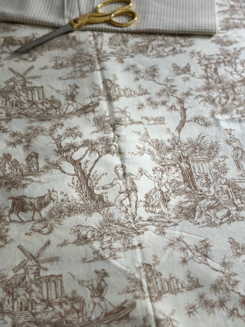 May include: Cream-colored fabric with a brown toile pattern depicting pastoral scenes, windmills, and figures. Gold scissors and a checkered fabric are visible at the top. This fabric is suitable for various sewing projects.