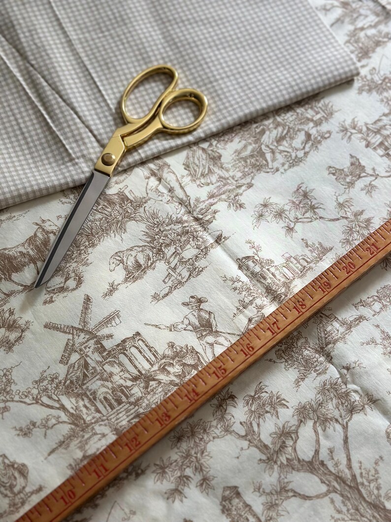May include: A collection of fabric and sewing tools. The image features a pair of gold scissors, a wooden ruler, and two types of fabric. One fabric has a brown toile pattern, and the other is a light gray gingham check.