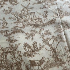 May include: Cream-colored fabric with a brown toile pattern. The design features pastoral scenes with windmills, figures in boats, goats, and other animals. The fabric has a vintage aesthetic, suitable for home decor or crafting projects.