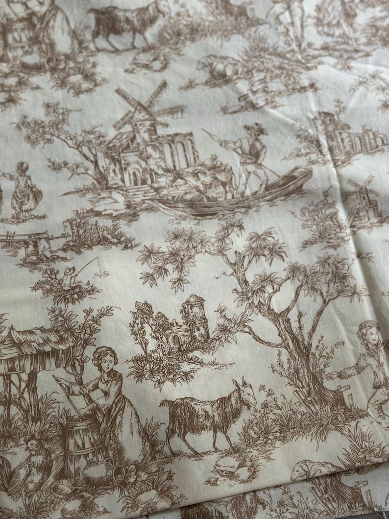 May include: Cream-colored fabric with a brown toile pattern. The design features pastoral scenes with windmills, figures in boats, goats, and other animals. The fabric has a vintage aesthetic, suitable for home decor or crafting projects.