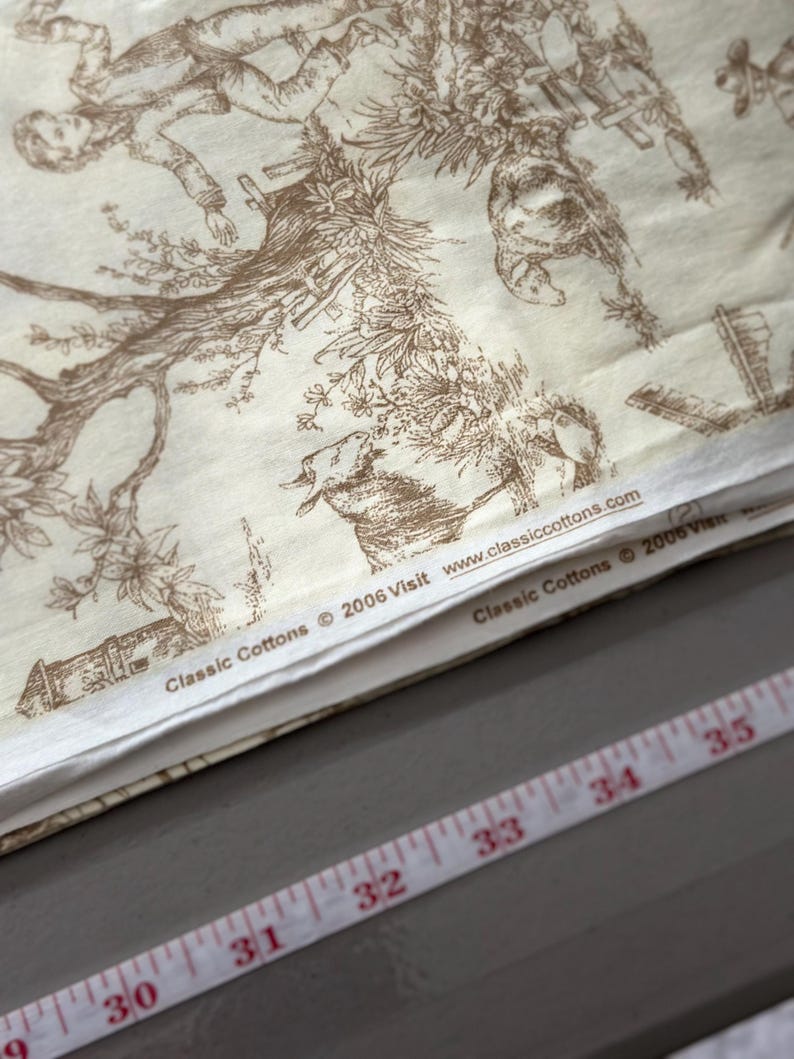 May include: Cream-colored fabric with a brown toile pattern featuring figures, trees, and buildings. The fabric has the text "Classic Cottons &copy; 2006 Visit www.classiccottons.com". A measuring tape with inch markings is visible.