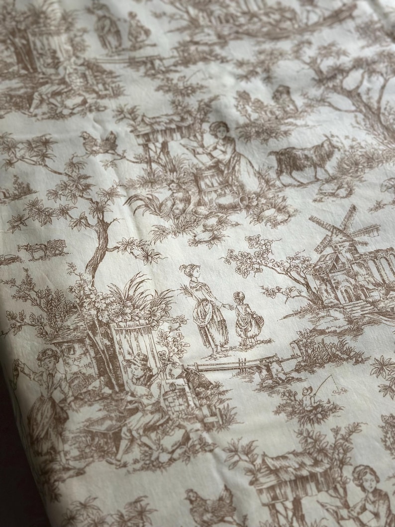 May include: Cream-colored fabric with a brown toile pattern depicting pastoral scenes. The design includes figures, buildings, trees, and animals, creating a detailed and classic aesthetic. The fabric is likely used for home decor or apparel.