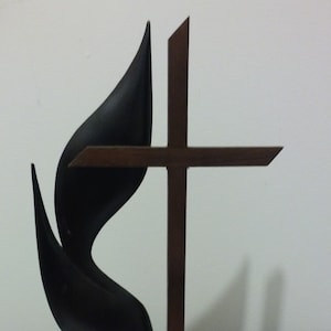 May include: A wooden base with a black flame and cross sculpture. The flame is stylized and the cross is simple.