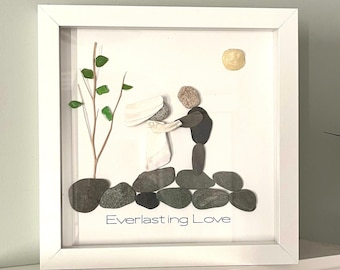 May include: A framed artwork made with small stones depicting a bride and groom standing on a rock formation with a small tree and the words "Everlasting Love" below.