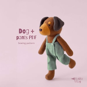 Op de afbeelding: Een handgemaakt bruin hondenspeelgoed met groene tuinbroek. De hond heeft een bruine snuit en oren, met de tekst "Dog + pants PDF Sewing pattern" aan de linkerkant. De hond staat op een roze achtergrond.