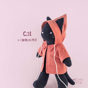 May include: A black plush cat toy wearing a terracotta-colored hooded jacket with white drawstrings. The text "Cat + clothes PDF" is visible on the left, and the text "Lucky Flag" is in the bottom right corner of the image.