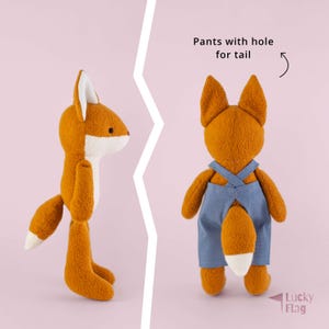 May include: A plush fox toy shown from the side and back. The fox has orange fur, a white chest, and a white-tipped tail. The back view shows the fox wearing blue overalls with a hole for the tail. Text reads: Pants with hole for tail and Lucky Flag.