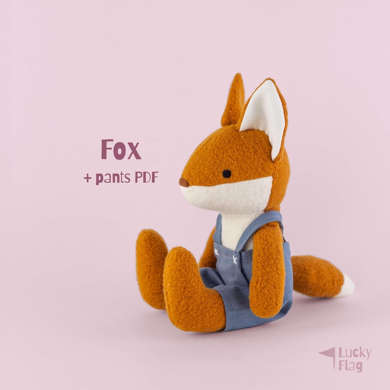 May include: A plush fox toy with orange and white fur, wearing blue overalls with white stitching details. The text "Fox + pants PDF" is printed to the left of the fox, and the text "Lucky Flag" is printed in the bottom right corner.