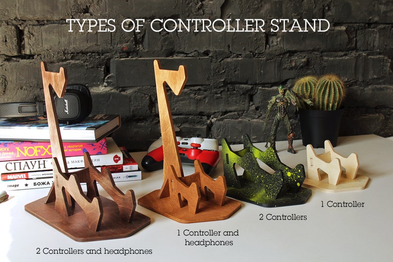 May include: Three different types of wooden controller stands. The first stand is brown and holds two controllers and headphones. The second stand is natural wood and holds one controller and headphones. The third stand is painted green and holds two controllers.
