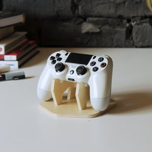 May include: A white PlayStation 4 controller is displayed on a wooden stand. The stand is a light brown color and has a hexagonal base.