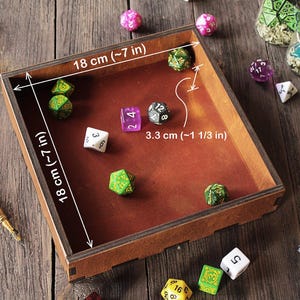 K&ouml;nnte beinhalten: Ein quadratisches W&uuml;rfeltablett aus Holz mit braunem Innenboden, das 18 cm mal 18 cm misst und eine H&ouml;he von 3,3 cm hat. Das Tablett enth&auml;lt mehrere mehrseitige W&uuml;rfel in verschiedenen Farben, darunter Gr&uuml;n, Lila, Wei&szlig; und Schwarz, sowie weitere verstreute W&uuml;rfel.