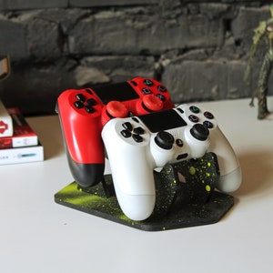 May include: Two video game controllers, one red and one white, are displayed on a black and yellow stand. The stand has a speckled design.
