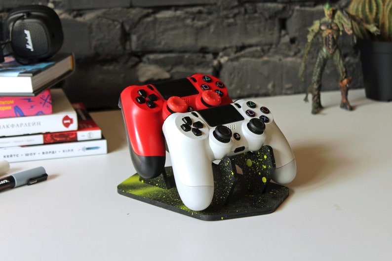 May include: Two video game controllers, one red and one white, are displayed on a black and yellow stand. The stand has a speckled design.