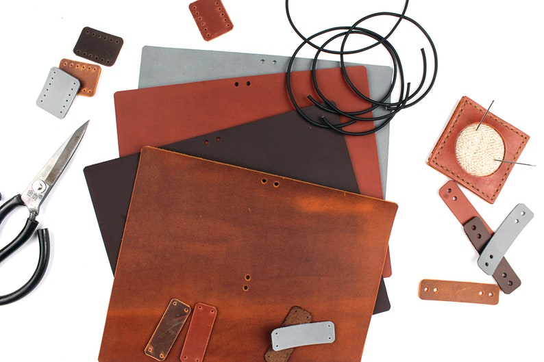 May include: A collection of leather pieces for crafting, including various sizes of brown leather squares, a brown leather rectangle, a gray leather rectangle, a black leather rectangle, a brown leather rectangle with holes, a brown leather rectangle with holes and a white thread, and a brown leather rectangle with holes and a white thread.