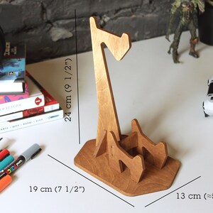 May include: Wooden headphone stand with a unique design. The stand is 9 1/2 inches tall, 7 1/2 inches wide, and 5 inches deep.