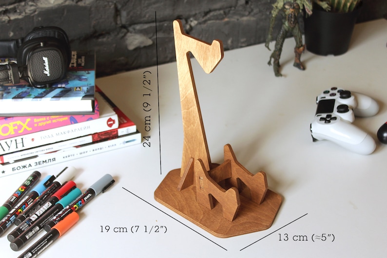 May include: Wooden headphone stand with a unique design. The stand is 9 1/2 inches tall, 7 1/2 inches wide, and 5 inches deep.