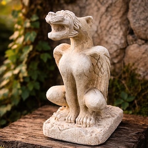 Peut inclure: Statue de gargouille en pierre avec des ailes, posée sur une surface en bois. La gargouille a la bouche ouverte, des ailes détaillées et est accroupie. La statue est de couleur beige clair, avec une surface texturée.