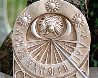 May include: A beige stone sundial with Roman numerals, a lion's head, crescent moons, and sun designs. The sundial has a metal gnomon and is likely used for outdoor garden decor. The sundial is approximately 12 inches in diameter.