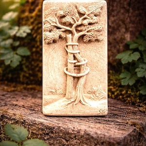 Peut inclure: Sculpture rectangulaire beige représentant un arbre avec un serpent enroulé autour du tronc. L'arbre a des feuilles et des branches détaillées. La sculpture est posée sur une surface en bois vieilli, avec un feuillage vert en arrière-plan.