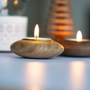 May include: Two wooden candle holders with a gold rim, each holding a lit tea light candle. The candle holders are on a white surface.