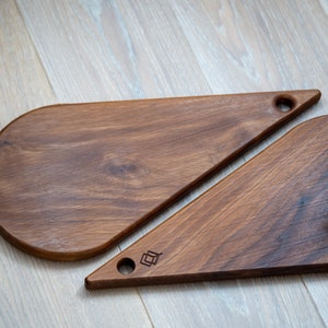 May include: Two wooden chopping boards shaped like teardrops. The boards are made from dark wood and have a smooth finish. One board has a small hole in the top for hanging.