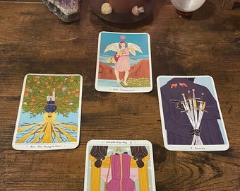 Puede incluir: Lectura de cartas del tarot con una vela encendida, una bola de cristal y cinco cartas extendidas sobre una mesa de madera. Las cartas son "El Colgado", "Templanza", "7 de Espadas", "El Hierofante" y "7 de Espadas".