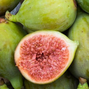 May include: A close-up of a group of green figs, one of which is cut open to reveal its pink interior and small seeds.