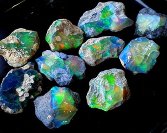 Puede incluir: Una colección de piedras de ópalo en bruto con una variedad de colores iridiscentes, incluyendo verde, azul y naranja. Las piedras están dispuestas sobre un fondo negro.
