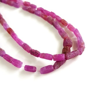 May include: A strand of pink ruby beads, each bead is faceted and has a rough, textured surface. The beads are strung on a clear thread.