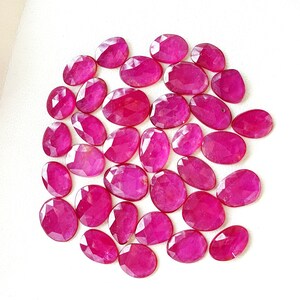 Puede incluir: Una colección de 25 piedras preciosas de rubí talladas en forma ovalada. Los rubíes son de color rosa intenso y tienen un alto pulido.