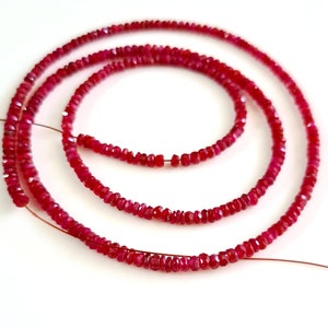 May include: A strand of ruby red gemstone beads, strung on a thin wire. The beads are faceted and have a slightly irregular shape.
