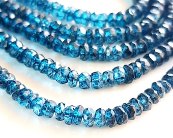 May include: A strand of blue topaz beads, faceted and with a slightly irregular shape. The beads are strung on a clear thread and are arranged in a loose, flowing pattern.