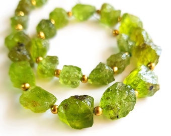 May include: A strand of green peridot gemstone beads with gold spacers. The beads are rough and irregular in shape, giving the necklace a natural and rustic look.