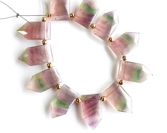 May include: A strand of faceted fluorite beads. The beads are a mix of purple, green, and clear, with gold-colored spacer beads. The beads are strung on a thin, dark string, and are arranged in a circular pattern.