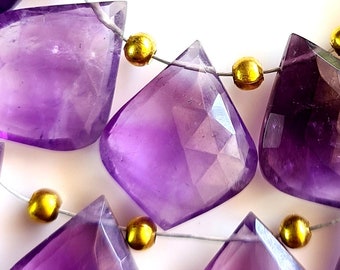 May include: A strand of amethyst gemstone beads with faceted, teardrop-shaped beads. The beads are strung on a silver wire with gold spacer beads.