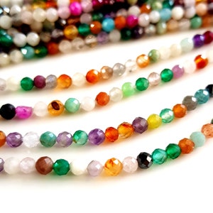 May include: Close-up of several strands of faceted gemstone beads in a variety of colors, including green, orange, purple, and white. The beads are strung together, creating a colorful and textured display. Ideal for jewelry making.